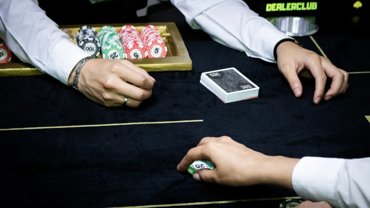 Manos de dealer y jugador en plena mano, junto al rack de fichas